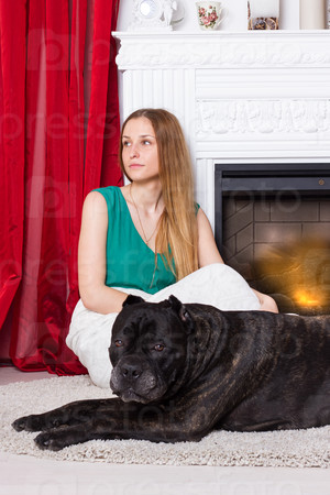 Girl in green dress sitting by the fireplace with a dog Cane Corso