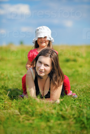 Mom and little daughter in the meadow in the green grass. Sunny summer day. Shallow depth of field. Selective focus on mother\'s face. Vertical shot.