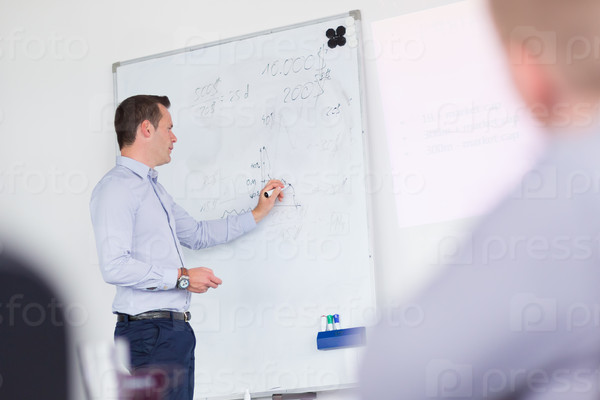 Businessman writing on whiteboard during his presentation on in-house business training, explaining business plans to his employees.