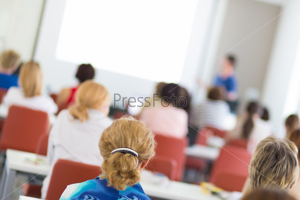 Speaker giving presentation in lecture hall at university. Participants listening to lecture and making notes, stock photo