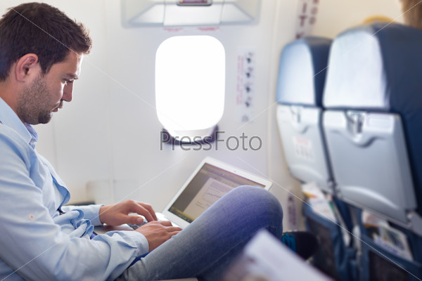 Casually dressed middle aged man working on laptop in aircraft cabin during his business travel. Shallow depth of field photo with focus on businessman eye.