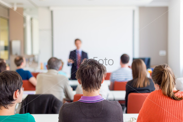 Speaker giving presentation in lecture hall at university. Participants listening to lecture and making notes. Copy space for brand on white screen, stock photo