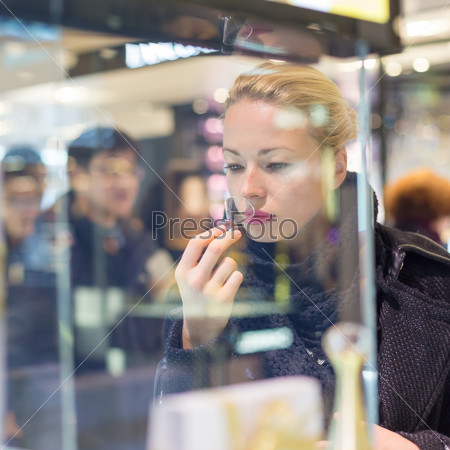 Beautiful blond lady testing and smelling perfume in a beauty store. Woman buying cosmetics in perfumery.