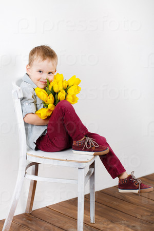 portrait of Smiling boy with a bouquet of yellow tulips flowers in hands standing near white wall