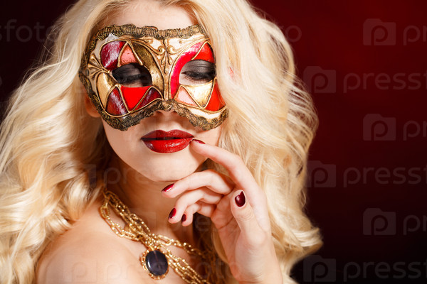 Beautiful young blonde woman in a red and gold mysterious venetian mask on dark background