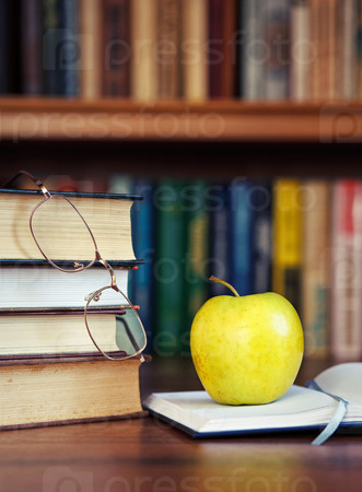 green apple on the open book with books and glasses