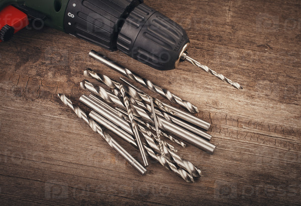 Drill and set of drill bits with screws on wooden background