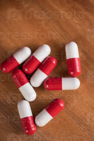 White and red pills on wooden background.