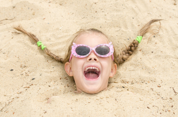 Funny five-year girl with glasses on a beach strewn on his head in the sand