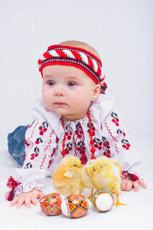 Happy little girl in the national Ukrainian costume with easter eggs and baby chickens in studio
