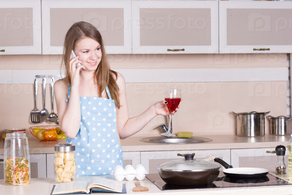 girl in the kitchen wearing an apron over his naked body with a glass of red wine on phone