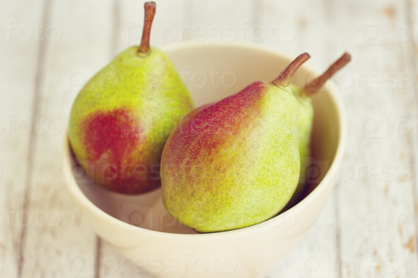Three pears in a bowl on a white table, stock photo