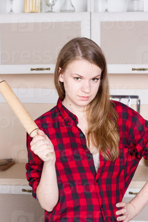 Girl with long flowing hair in a red men\'s shirt with a rolling pin in the kitchen. Vertical framing
