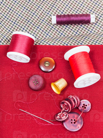 dressmaking still life - top view of bobbins with sewing thread, buttons, thimble, needle on red cloth