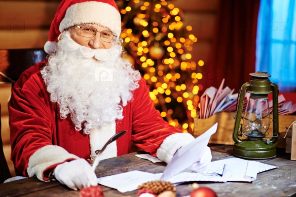 Santa Claus looking at camera while reading Christmas letter
