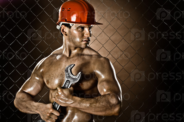 the beauty muscular worker  man, in  safety helmet  with big wrench  in hands, on netting fence background