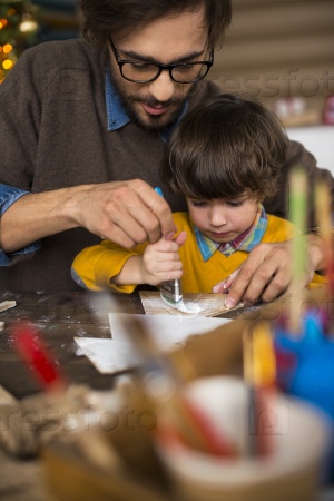 Young man and his son painting xmas decorations with white gouache