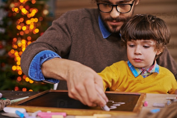 Young man and his son drawing xmas tree on blackboard with chalk