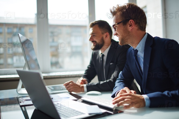 Smiling businessman and his colleague looking at computer monitor at meeting, stock photo