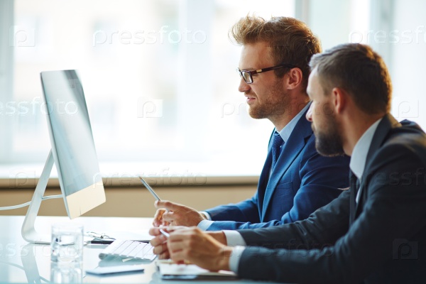 Confident businessman pointing at computer monitor during explanations