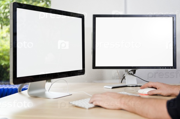 Two computer monitors with a white screen on a desk, with a man\'s hands on a keyboard in an office, suited for mock-ups and presentations, with plenty of copy space for your designs