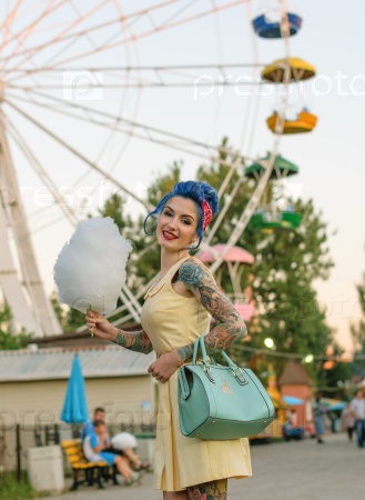 Girl with a tattoo with cotton candy in the hands of an amusement park on the background of traits kolesa.Retro style.