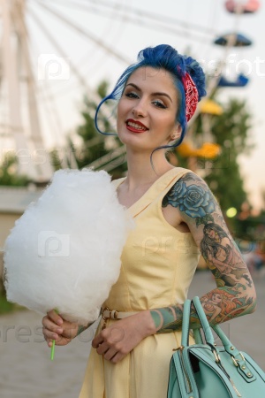 Girl with a tattoo with cotton candy in the hands of an amusement park on the background of traits kolesa.Retro style.