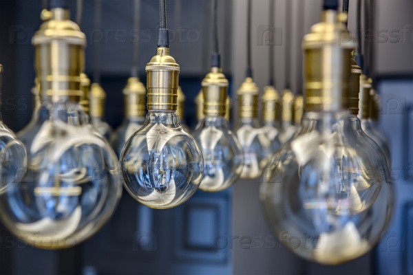 Edison lamps suspended from the ceiling in a regular geometric sequence. One lamp in focus. The rest of the optical out of focus.