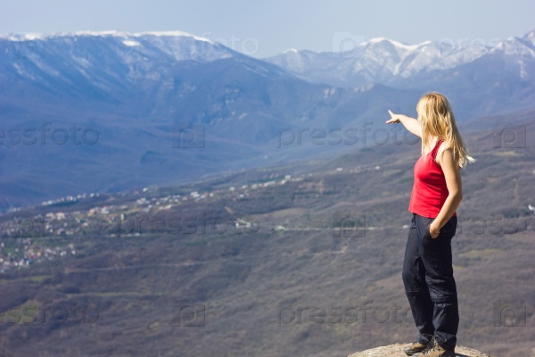 girl standing and showing on a cliff in the mountains