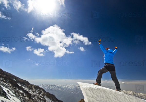 happy man in jacket with hands-up standing on a cliff in mountains at sunrise