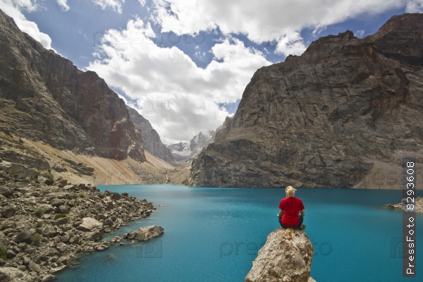 girl in red t-shirt sitting near blue mountain lake