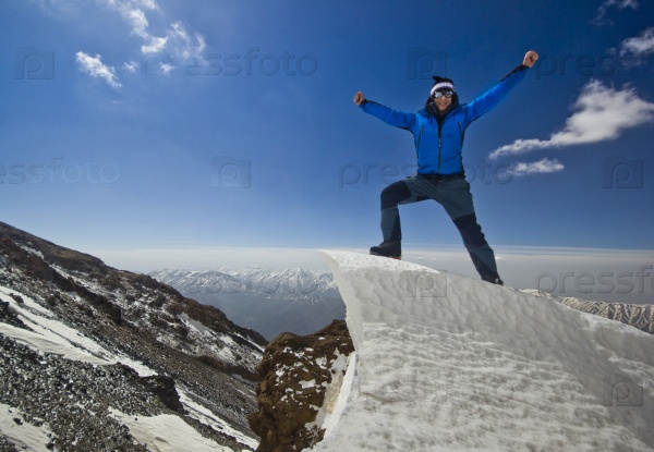 happy man in blue jacket with hands-up standing on a cliff in mountains at sunrise