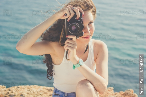 Tourist smiling slim girl making photo of the nature by old camera on the peak of mountain over sea background, stock photo