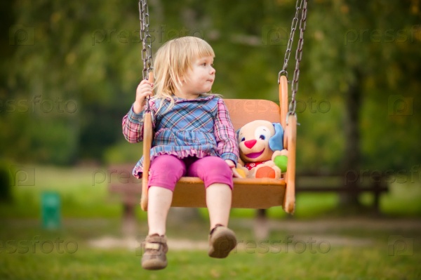 Девочка на качелях с плюшевой игрушкой на площадке в парке