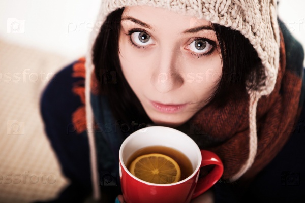 A sip of hot coffee in the winter. A girl in a knitted hat holding a red cup of tea with lemon