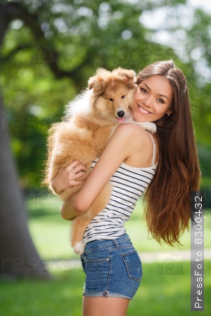 woman beautiful young happy with long dark hair in striped sweater holding dog. Young woman playing with Collie puppy outdoors in the park.