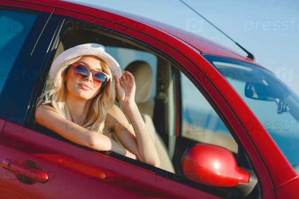 blonde beautiful woman in sunglasses and white hat sitting in red car by the sea. Sea view. Vacation concept. Happyness. Freedom. road trip on beautiful sunny summer day
