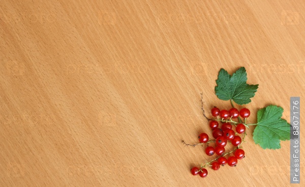 Twigs ripe ripe red currant with two green leaves lying in the corner of the wooden surface.
