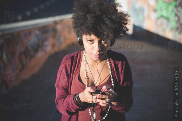 beautiful black curly hair african woman listening to music with headphones in town