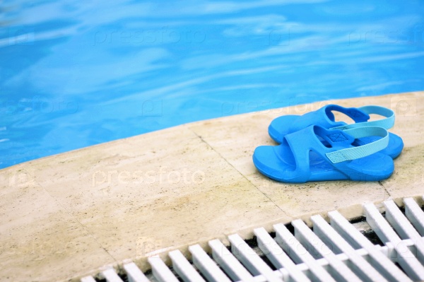 The image of a small pair of children\'s rubber footwear for trips to the beach and in the pool. Specialized Shoe is on the edge of the pool.