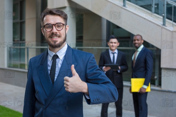 Portrait of multi ethnic business team holding their thumbs up. Three  man hand showing thumbs up against the backdrop of the city. The one man is European, other is Chinese and African-American.