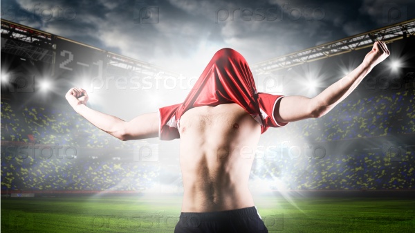 soccer or football player is celebrating goal on stadium with his jersey on head