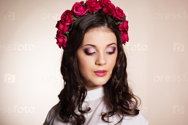 Fashion portrait of cute teenager girl with nice makeup is wearing white blouse and red roses wreath on her head