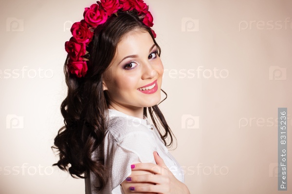Fashion portrait of happy pretty brunette girl is wearing white blouse and red roses wreath.