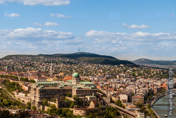 Cityscape of Budapest in warm sunlight with Buda Castle visible through trees of Gellert Hill.