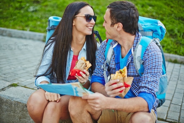 Young couple with backpacks having snack in urban environment