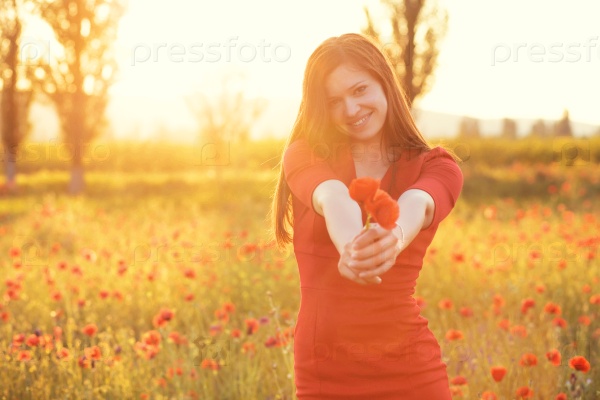 Young woman giving flower in sunlight in poppy field