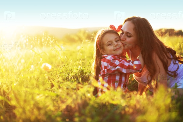 Mom and her 6 years old child playing in spring field. Mother kissing daughter, stock photo