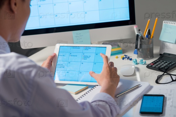 Entrepreneur using calendar on digital tablet, view over the shoulder