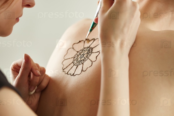 Mehndi master drawing with henna on model\'s back